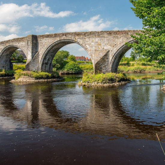 a historic bridge in verdant settings reflected in the rivers surface