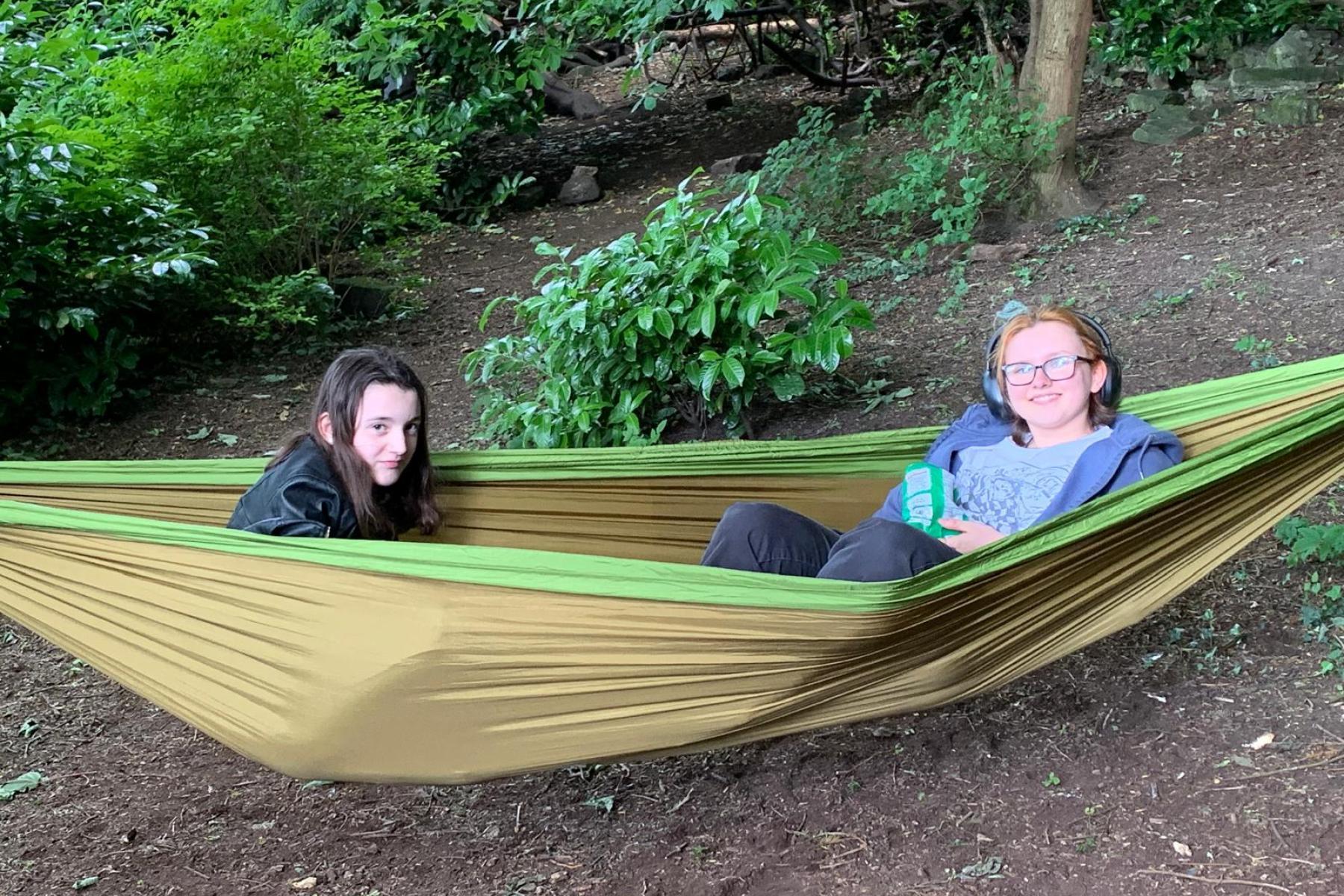 Two young people in a hammock in the woods smiling into camera