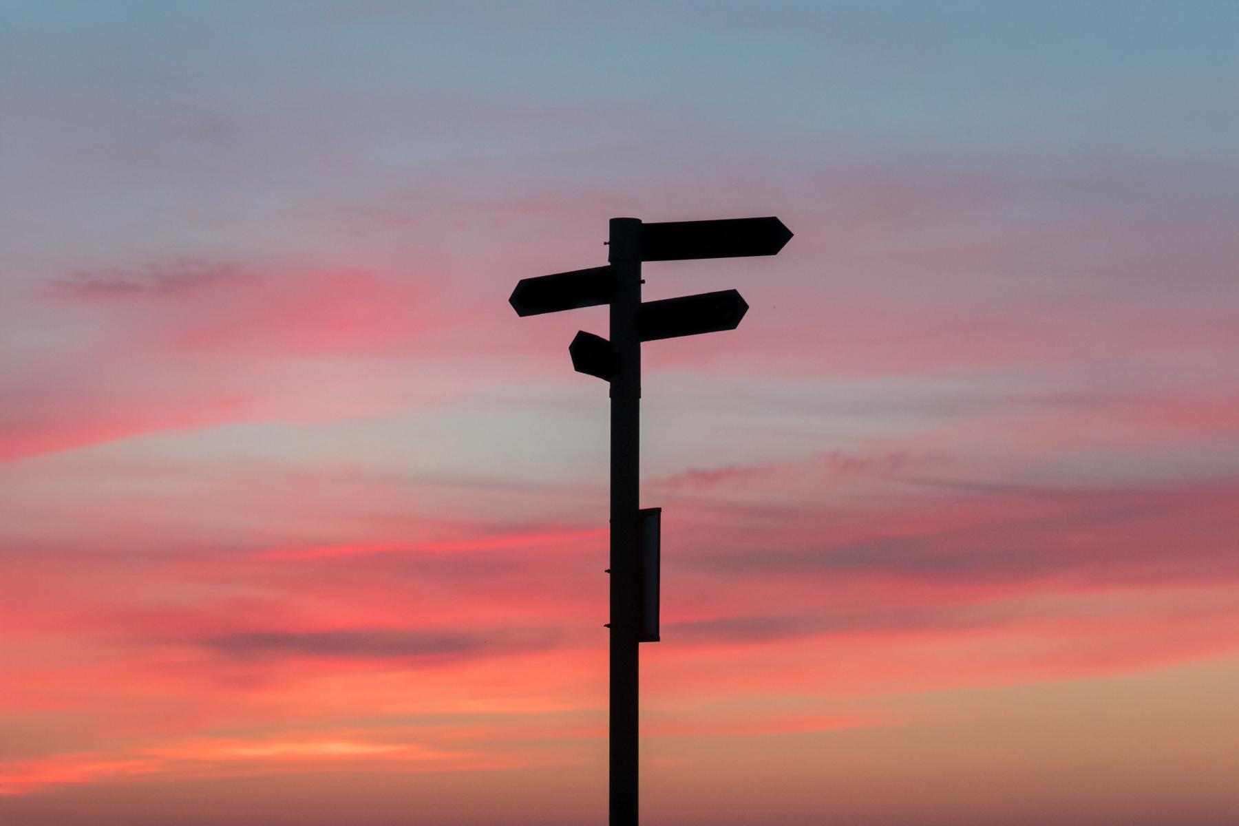 Multi-direction street sign silhouetted against a clear sunset sky