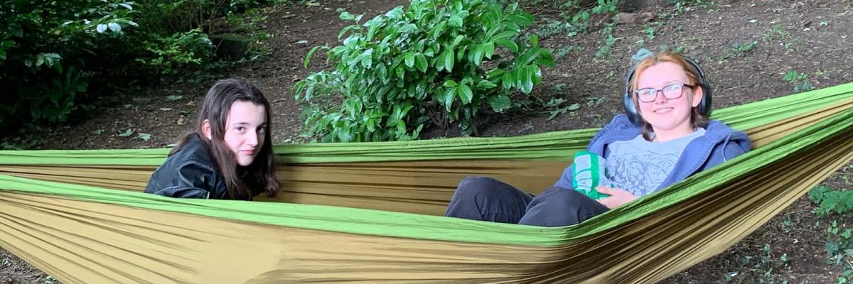 Two young people in a hammock in the woods smiling into camera