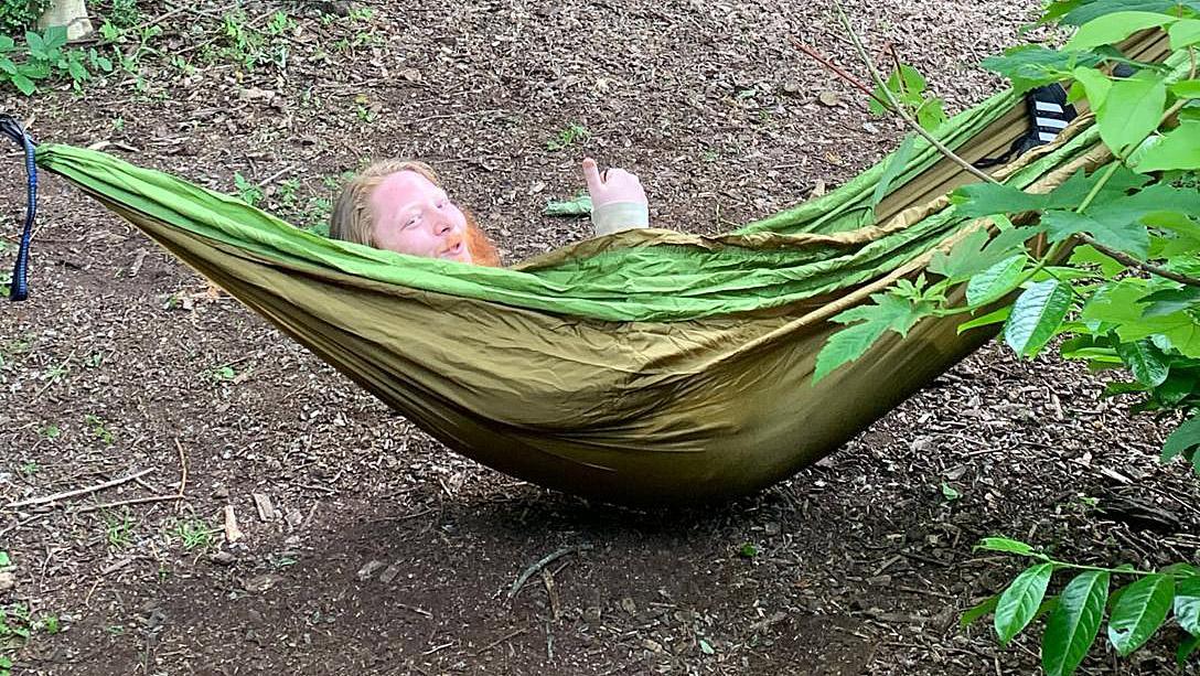 Young man in hammock in woods grinning and giving a thumbs up sign