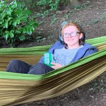 Young person in a hammock in the woods smiling into camera