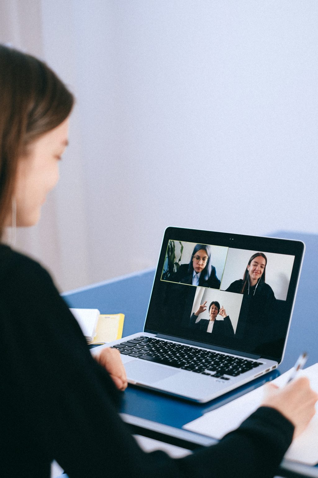 Woman taking notes during a video call with three colleagues on a laptop