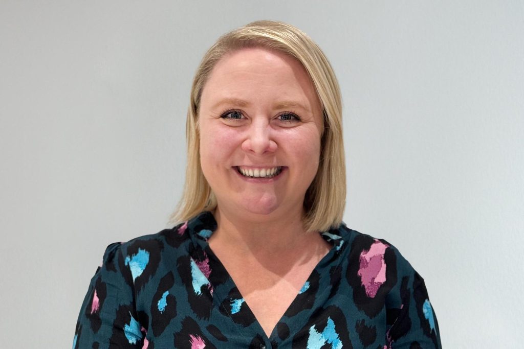 Holly Smith smiling in a teal leopard-print blouse