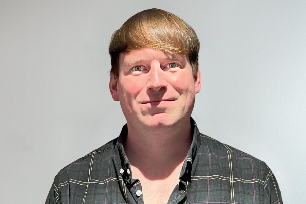 Jon Dimmick smiling in a checked shirt