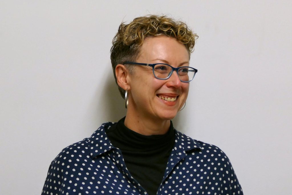Louise Bowen smiling, with short curly hair and blue glasses