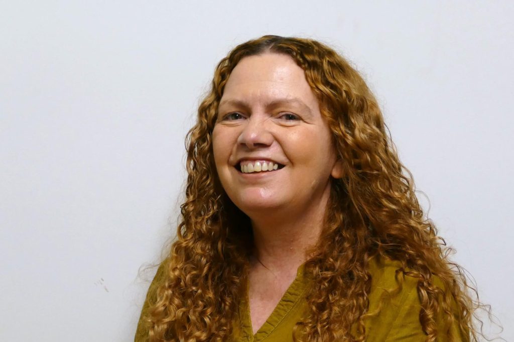 Maxine Dinnes smiling, with long curly auburn hair