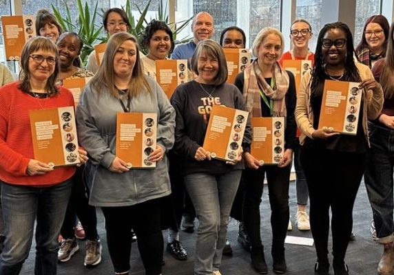 Smiling group of people holding copies of an orange Iriss publication